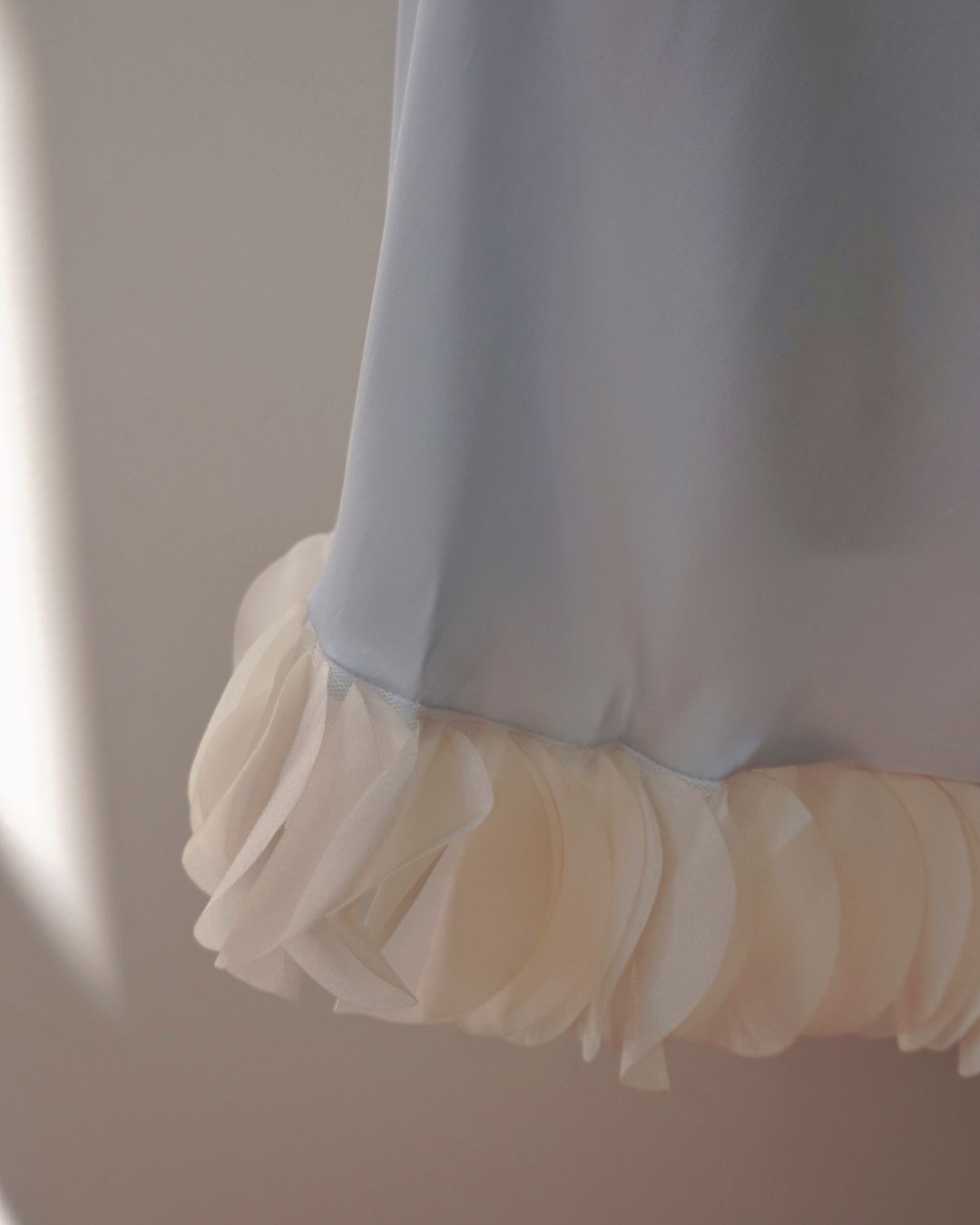 Close-up of a light blue garment with a white ruffled hem against a neutral background