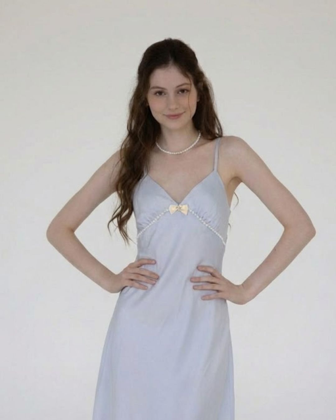 Woman wearing a light blue dress with a gold bow detail against a white background