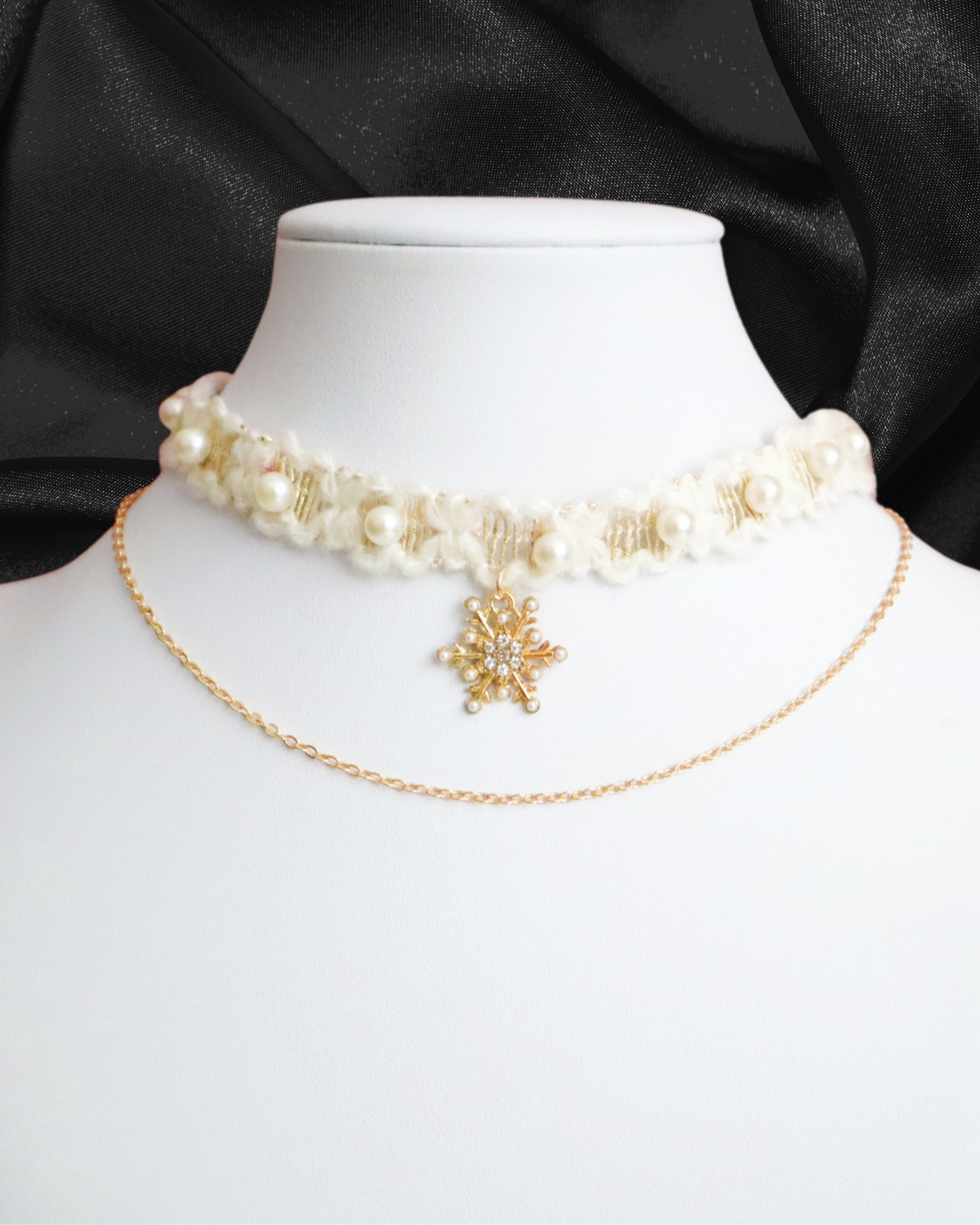 Pearl choker necklace with a gold chain and snowflake pendant on a mannequin against a black satin background.