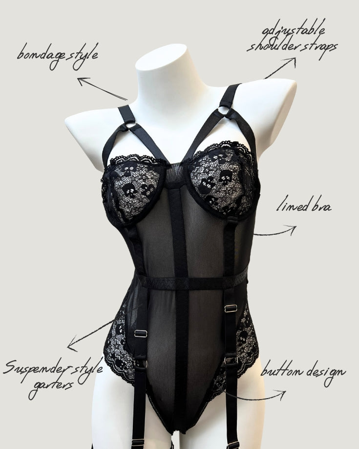 front view of Ravenbite Bodysuit in black mesh with skull lace cups and built-in garter straps. Strappy and structured silhouette.