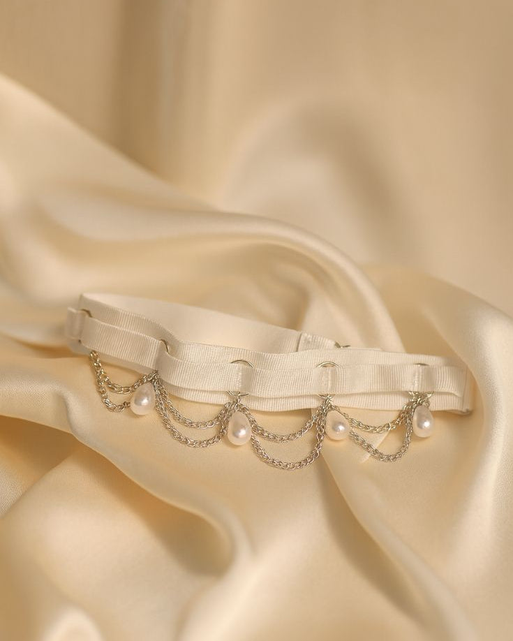 Decorative leg harness with pearls and chains on a beige satin background