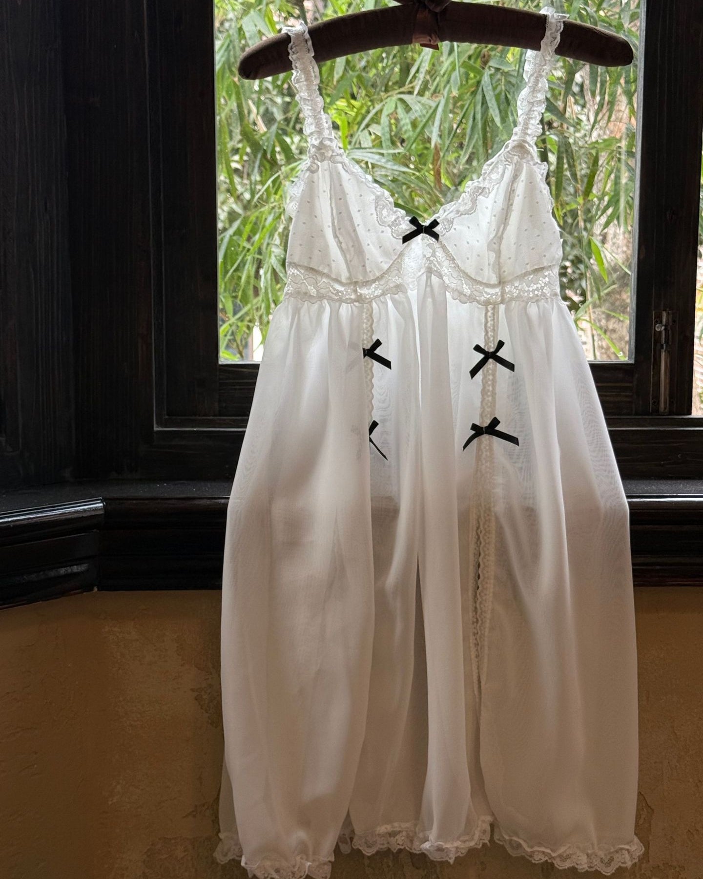 White dress with black crosses on a hanger in front of a window with greenery.