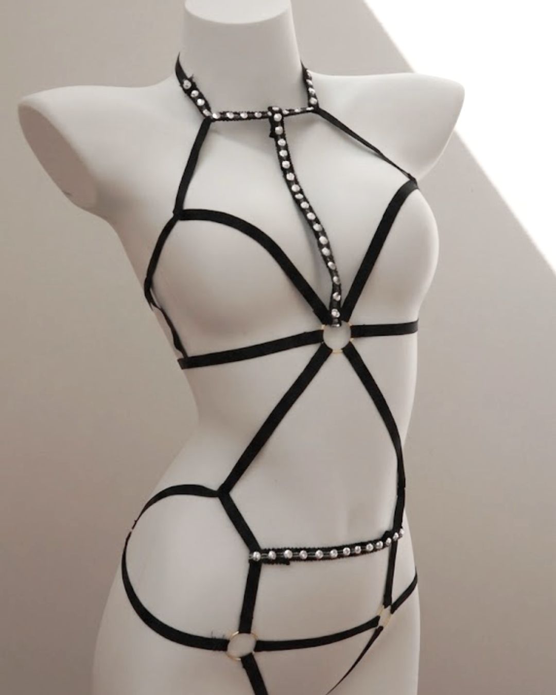 Black strappy bondage harness lingerie  with bead details on a mannequin against a neutral background