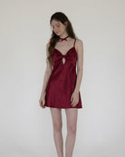 Woman wearing a burgundy satin dress against a plain background