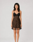 A woman modeling a short black and brown leopard-print chemise with a black lace bodice and sheer black tulle hem, photographed against a light gray studio background.