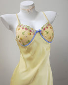 Yellow nightgown with floral embroidery on a mannequin against a gray background
