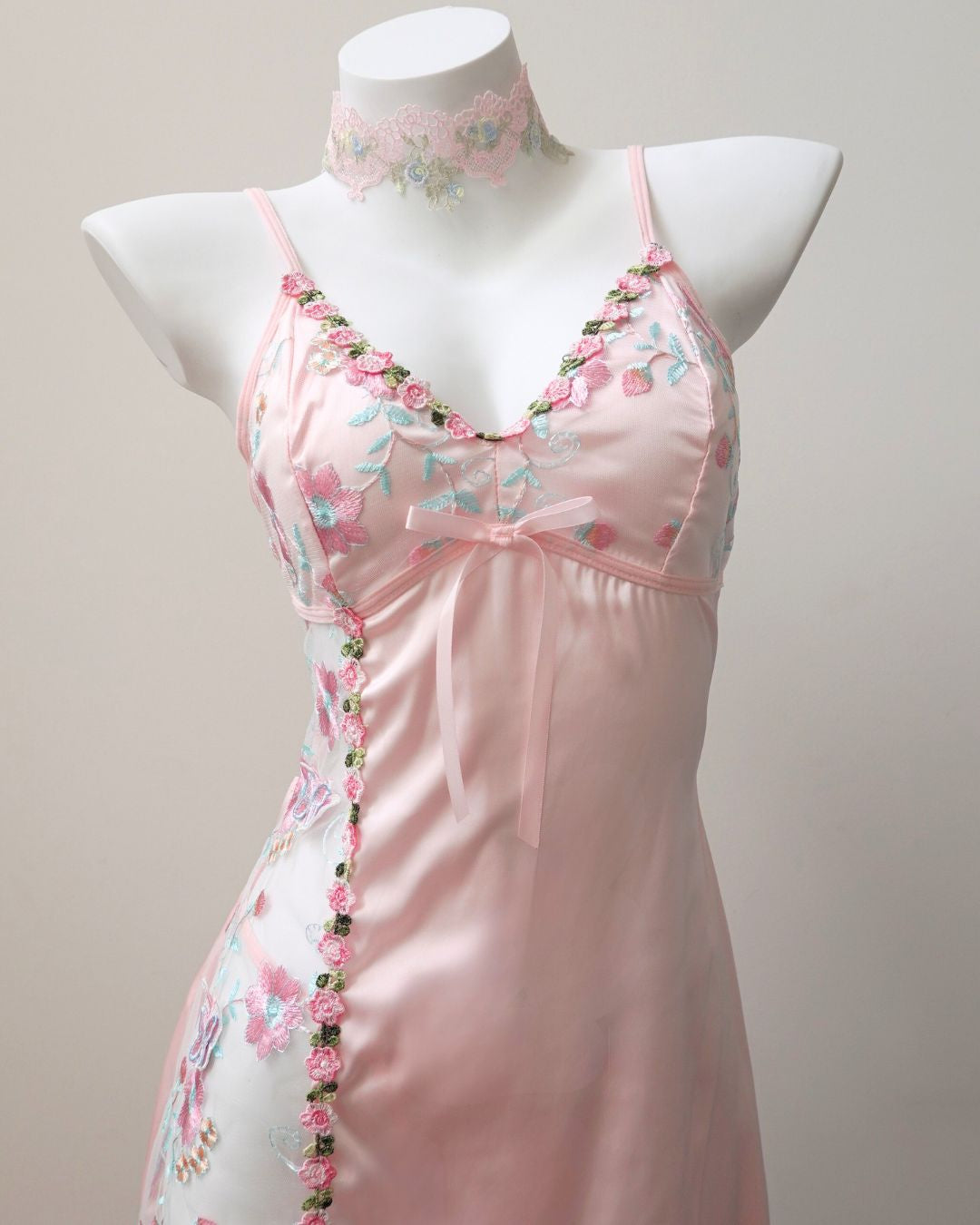 Pink satin nightgown with floral embroidery on a mannequin against a plain background