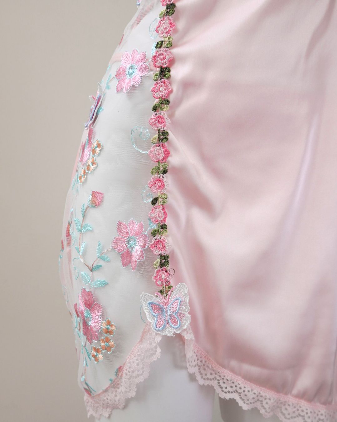 Close-up of a pink garment with floral and butterfly embroidery on a plain background