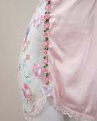 Close-up of a pink garment with floral and butterfly embroidery on a plain background