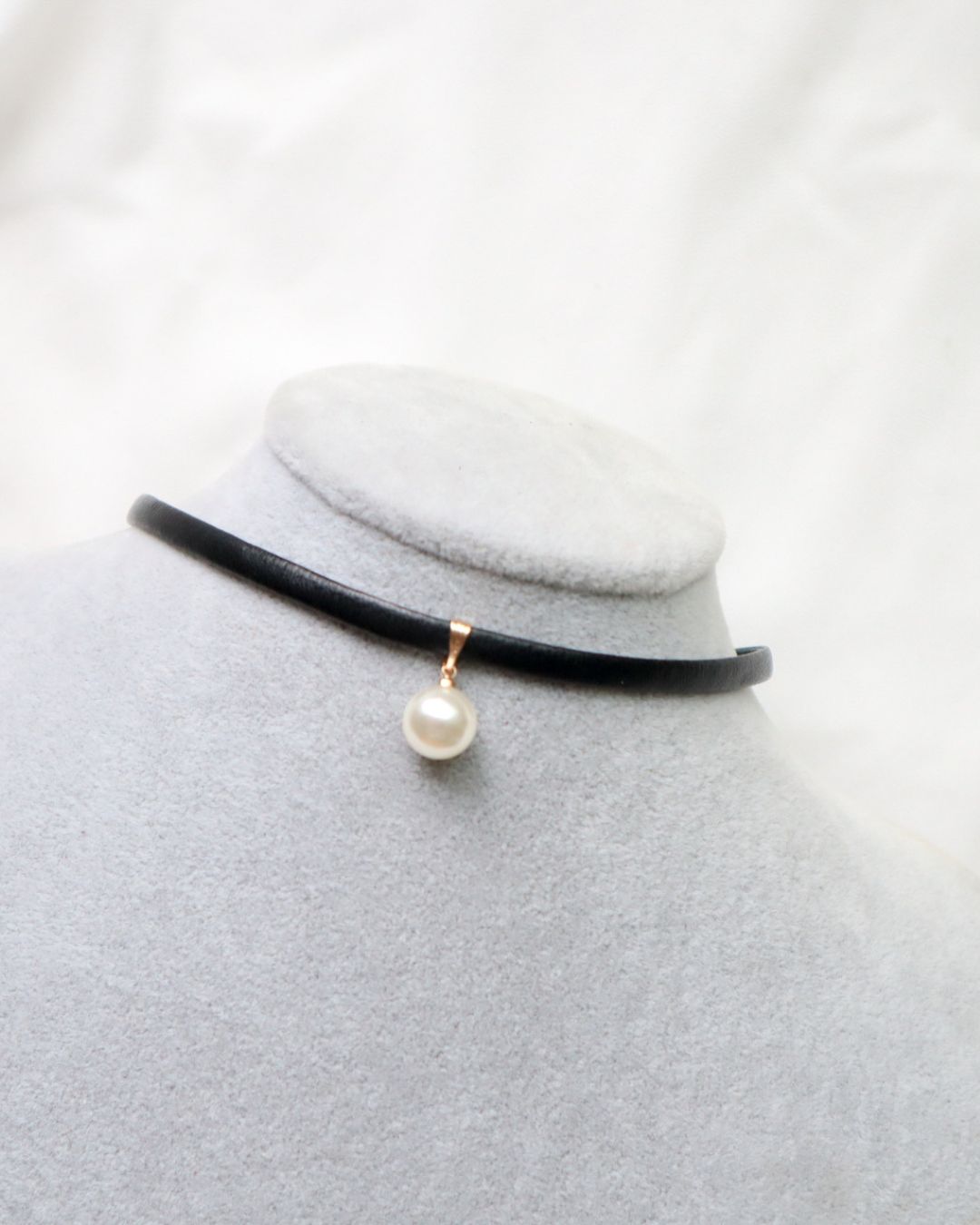 Black choker necklace with a pearl pendant on a mannequin bust against a white background