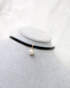 Black choker necklace with a pearl pendant on a mannequin bust against a white background