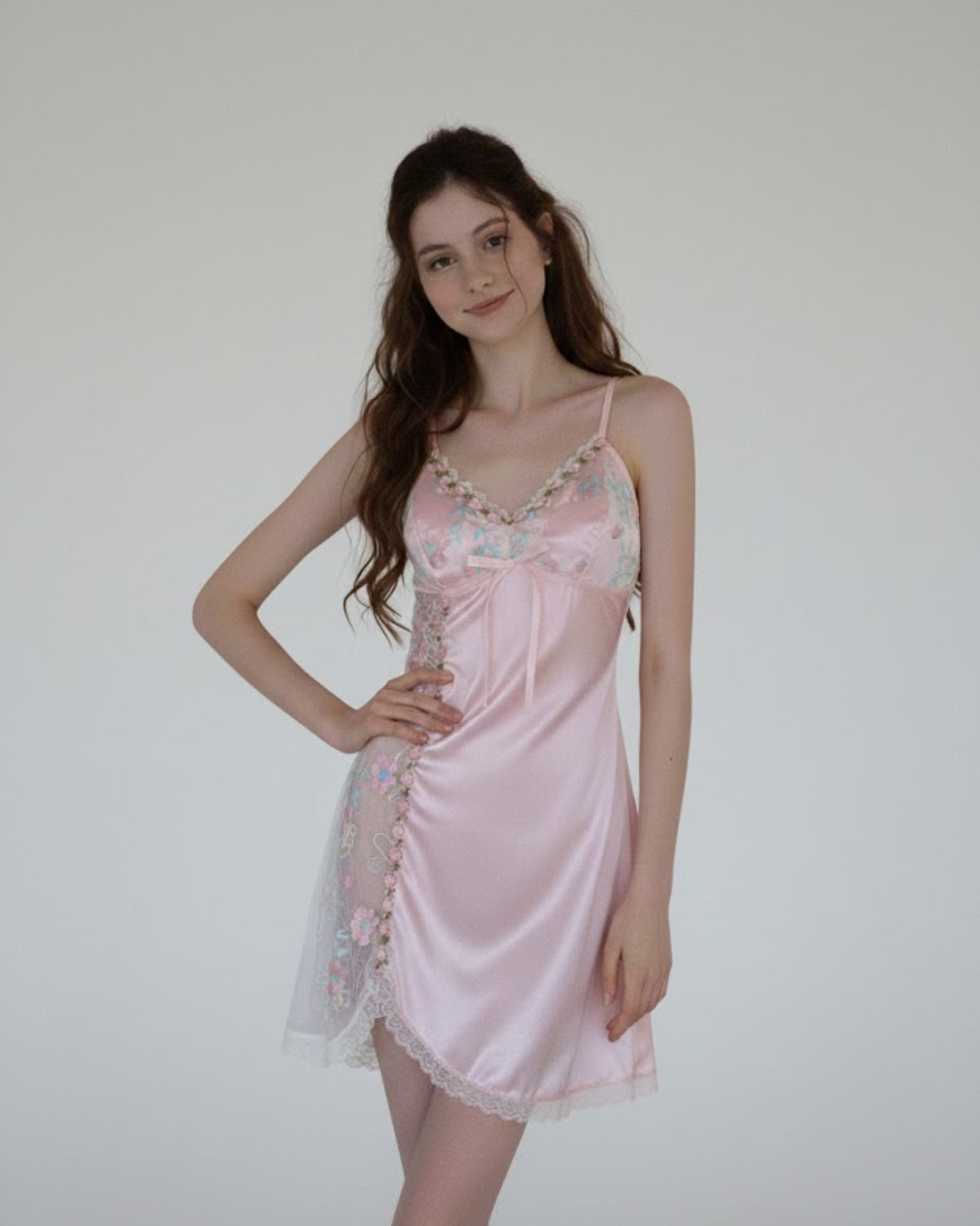 Woman wearing a pink satin nightgown with floral lace details against a plain background