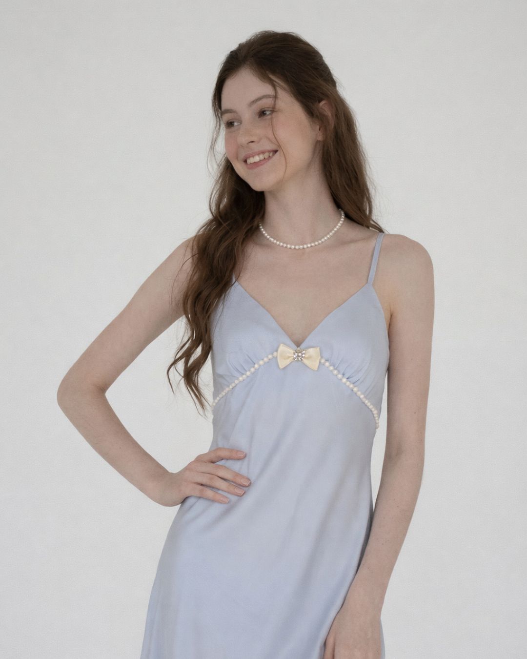 Woman wearing a light blue dress with a bow detail on a white background