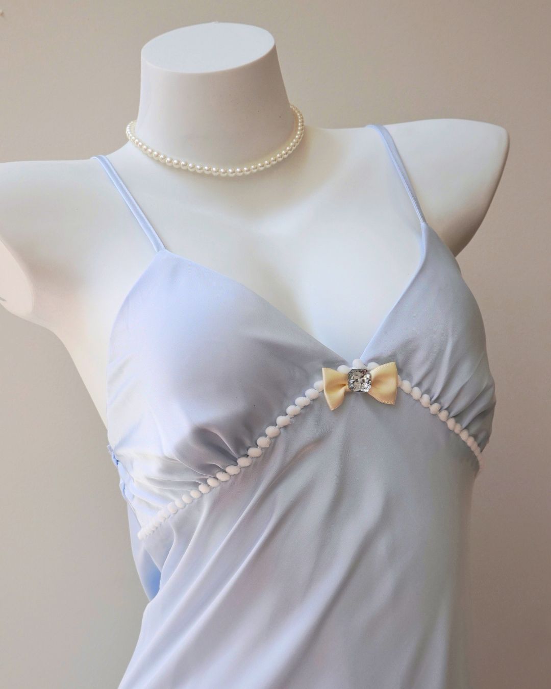Mannequin wearing a light blue nightgown with a bow and pearl details on a plain background