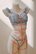 Pink harness worn over lingerie, featuring body-conforming straps and silver ring accents – styled with blue bra and tulle skirt