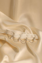 Decorative leg harness with pearls and chains on a beige satin background
