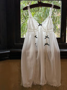 White dress with black crosses on a hanger in front of a window with greenery.